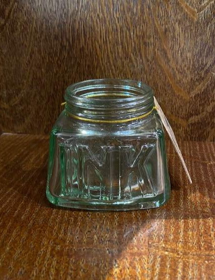 Image shows a glass pen storage pot that resembles an old empty jar of ink with the word ink stamped into the glass on one side.