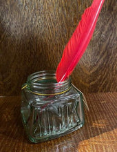 Load image into Gallery viewer, Image shows a glass pen storage pot that resembles an old empty jar of ink with the word ink stamped into the glass on one side. There is a few feather quill pen sitting in the jar.
