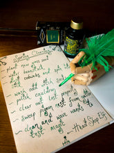 Load image into Gallery viewer, Image of Fourth Leaf of Clover green and gold shimmer ink displayed with a wooden mannequin gand and feather quill poised over paper with green cursive writing