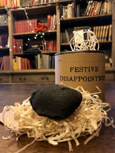 Load image into Gallery viewer, Image shows a tin of Festive Disappointment with kraft paper label, lid is open showing wood wool shreds and a lump of black coal