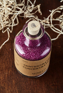 Top view image of Concentrated Concentration otherwise known as scented, purple bath salts in a glass bottle with cork