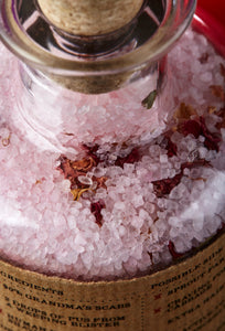 Close up view of Grandma's Scabs potion bottle of pale pink bath salts and dried rose petals in glass bottle with cork.