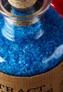 Close up image of Extract of Genius, otherwise known as scented, blue bath salts in a glass bottle with cork