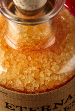 Load image into Gallery viewer, Close up image of Eternal Ugliness otherwise known as scented, orange coloured bath salts in a glass bottle with cork
