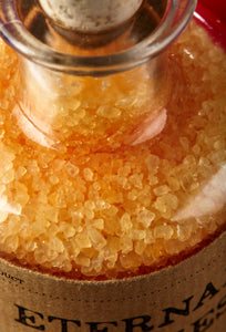 Close up image of Eternal Ugliness otherwise known as scented, orange coloured bath salts in a glass bottle with cork