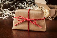 Load image into Gallery viewer, Image of a wrapped soap slice in kraft brown paper tied with red bakers twine in a bow, this is how it will be packaged for delivery.