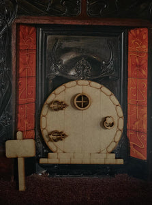 Image shows a round edition fairy door stuck onto a background of a fireplace. Accessories of window frames, decorative hinges and door knocker, and a standing sign are also included in the image.