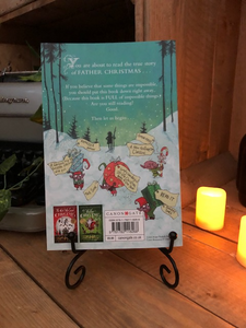 Image of the back cover of the paperback book called A Boy Called Christmas stood on a book stand with candles
