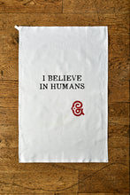 Load image into Gallery viewer, Image shows the Giant Handkerchief unfolded to display slogan printed in black on white cotton tea towel. Slogan reads 'I BELIEVE IN HUMANS' with the Grimm & Co red 'G' monogram underneath.