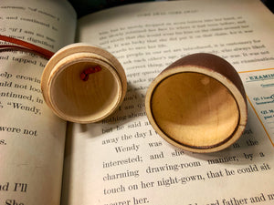Image shows A Kiss wooden acorn-shaped bauble in two halves displayed open to show the hollowed out inside with space to store messages, trinkets and small gifts. Acorn sat on open pages of the book of Peter Pan.