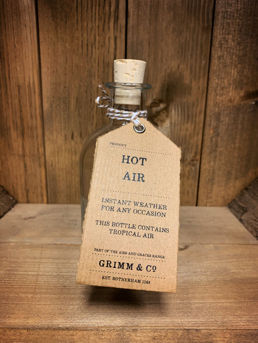 Image of the Hot Air bottle from the Airs and Graces range: An empty glass potion bottle with cork. The bottle has a kraft tag around the neck, reading: Hot Air. Instant weather for any occasion. This bottle contains tropical air..