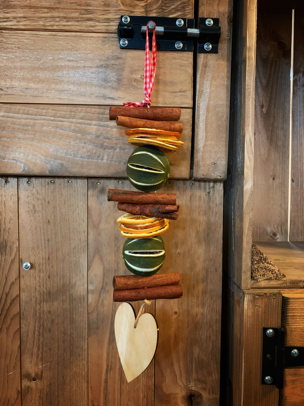 Image shows the Scents of the Season hanging garland Heart variant with dried whole limes with orange slices and cinnamon sticks with a wooden heart at the bottom
