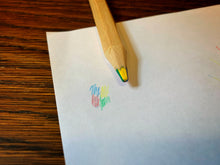 Load image into Gallery viewer, Image shows a close up of the lead in a Rainbow Word Wand. The pencil is resting on a piece of white paper, next to a small scribbled example of the four included colours that make up the lead: blue, yellow, red, and green.
