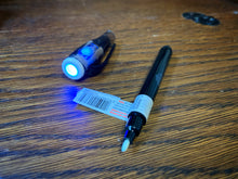 Load image into Gallery viewer, Image shows a close up view of the Invisible Ink Pen with the lid removed and the UV light switched on.