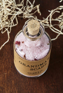 Top view of Grandma's Scabs potion bottle, a glass bottle and cork of pale pink bath salts and dried rose petals.