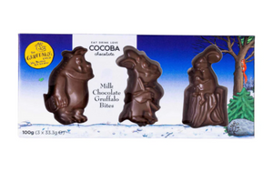 Image shows a flat lay of the Gruffalo Character Bites both in and out of their box. The box is placed above. The box is decorated with illustrations from the Gruffalo's Child, and has three clear windows in the character shape showing the chocolate inside. From left to right: the Gruffalo, the Gruffalo's Child, and the Mouse. 