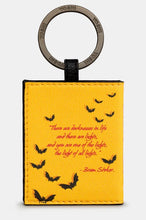 Load image into Gallery viewer, Image shows the back of the Dracula yellow PU leather keyring with a stamped metal ring branded with YOSHI. It is printed with a quote from the famous classic - &#39;There are darknesses in life, and there are lights, you are one of the lights, the light of all lights.&#39; Bram Stoker, text is printed in red with black bats surrounding the quote.