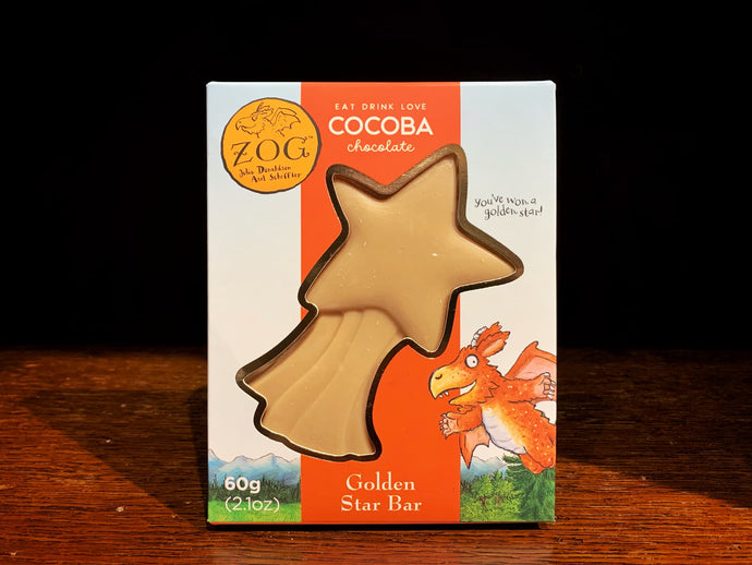 Image showing the Zog Gold Star Bar in its packaging The box is square, with an illustration from the book Zog on the front of a pale blue sky and grass/mountains, and Zog the Dragon in the lower right corner. In the middle of the box is a clear window in a shooting star shape, where you can see the caramel chocolate star. 