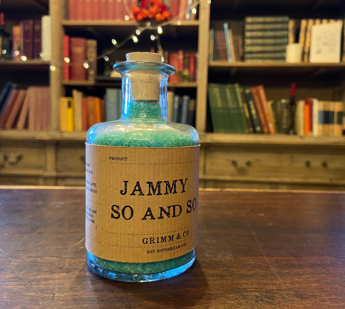 Image of a glass potion bottle filled with pale blue bath salts. The bottle label reads: Jammy So and So.