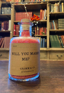 Image of a glass potion bottle filled with red bath salts. The bottle label reads: Will You Marry Me?