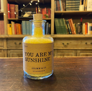Image of a glass potion bottle filled with yellow bath salts. The bottle label reads: You Are My Sunshine