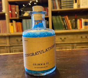 Image of a glass potion bottle filled with deep blue bath salts. The bottle label reads: Congratulations!