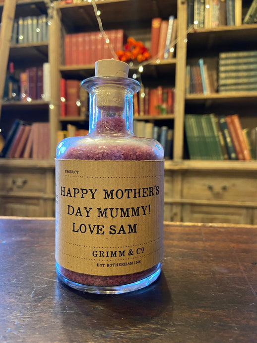 Image of a glass potion bottle filled with purple bath salts. The bottle label reads: Happy Mother's Day Mummy! Love Sam.