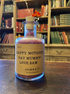 Image of a glass potion bottle filled with purple bath salts. The bottle label reads: Happy Mother's Day Mummy! Love Sam.