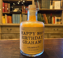 Load image into Gallery viewer, Image of a glass potion bottle filled with orange bath salts. The bottle label reads: Happy 900th Birthday Graham!