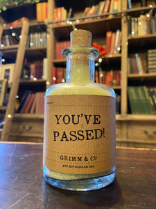 Image of a glass potion bottle filled with pale green bath salts. The bottle label reads: You've Passed!