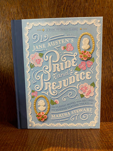 Image shows the front cover of the book Pride & Prejudice - A Book to Table Classic. The cover is pastel blue with a navy blue linen spine. There are illustrations of cameos of MR. Darcey and Elizabeth Bennett and icing sugar flowers decorating the cover. The text is white.