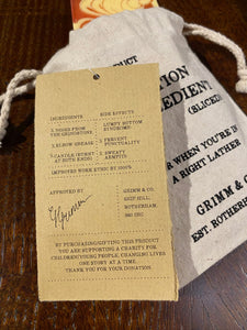 Image shows a white linen drawstring pouch with a Human Blood, Sweat & Tears soap bar poking out the top and a kraft label showing the faux ingredients and side effects.