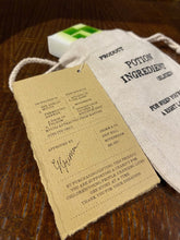 Load image into Gallery viewer, Image shows a cream linen drawstring bag with a Goblin Mucus soap bar and a kraft label showing the faux ingredients and side effects.