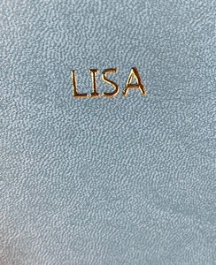 Image shows he name 'LISA' embossed onto the light blue journal with gold foil.