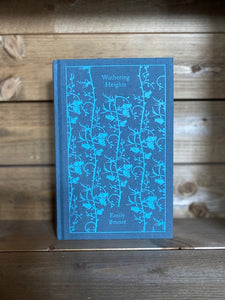 Image of the Penguin clothbound classic Wuthering Heights featuring a dusky blue-grey background with a blue repeat printed pattern of rose buds and thorny stems winding up the cover.