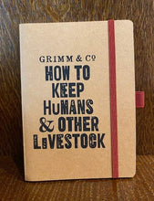 Load image into Gallery viewer, Image shows a kraft card notebook displaying the slogan &#39;Grimm &amp; Co. HOW TO KEEP HUMANS &amp; OTHER LIVESTOCK&#39;. The notebook has a red elastic closure and pen loop.