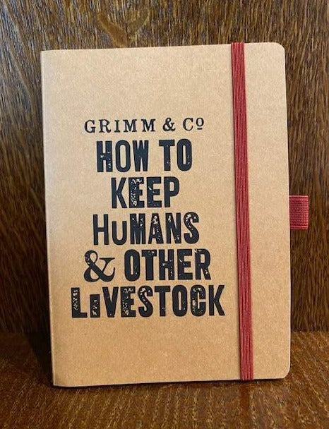 Image shows a kraft card notebook displaying the slogan 'Grimm & Co. HOW TO KEEP HUMANS & OTHER LIVESTOCK'. The notebook has a red elastic closure and pen loop.