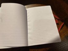 Load image into Gallery viewer, Image shows an open notebook with lined pages with a red elastic pen loop and closure seen on the right-hand side of the open book.