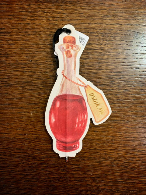 Image shows an illustrated flat paper pen in the shape of a corked bottle with red potion and illustration of a label saying Drink Me in gold foil.
