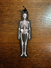 Load image into Gallery viewer, Image shows an illustrated flat paper pen shaped like a skeleton with a black background.