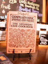 Load image into Gallery viewer, Image of the Cooking With Magic, Sprinkles and Friends cookbook. Book is coloured peach with black illustration of food items featuring title in black text.