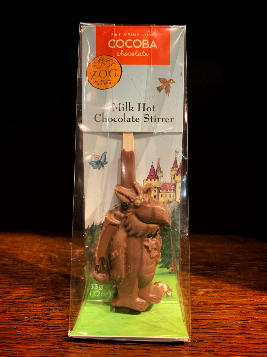Image shows the Zog milk chocolate stirrer spoon in its packaging with an illustration from Zog. Milk chocolate stirrer spoon is in the shape of the Zog the dragon.