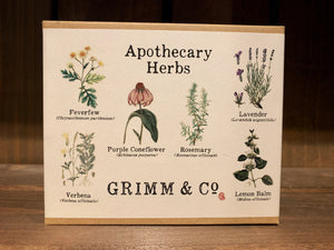 Image shows the box for the Apothecary Herbs seed collection. The box is a small, flat, rectangular 5 x 4 inch box made of kraft card, and has a white label folded over and underneath. The label has 'Apothecary Herbs' printed at the top, and 6 illustrations of the flowers/herbs contained within, with both common and scientific names listed underneath. The Grimm & Co. logo is printed at the bottom. 