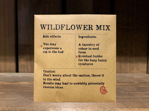Image shows a packet of Wildflower Mix seeds. It is a square, flat, kraft brown paper packet., with black text printed in Appareo font. It says Wildflower Mix at the top, with magical ingredients and side effects underneath, and a magical 'caution' at the bottom. 