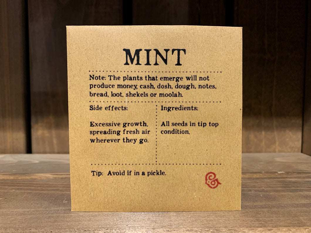 Image shows a packet of Mint seeds. It is a square, flat, kraft brown paper packet., with black text printed in Appareo font. It says Mint at the top, with magical ingredients and side effects printed underneath, and a magical 'caution' at the bottom.