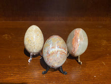 Load image into Gallery viewer, Image shows three marble eggs in natural stone colours sat on plastic stands.