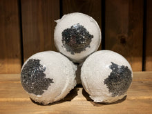 Load image into Gallery viewer, Image shows three/four Spare Eye bath bombs stacked in a pyramid shape. They are round and white, with a black charcoal circle in the centre - resembling large eyeballs. They are wrapped in clear plastic.