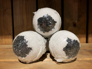Image shows three/four Spare Eye bath bombs stacked in a pyramid shape. They are round and white, with a black charcoal circle in the centre - resembling large eyeballs. They are wrapped in clear plastic.