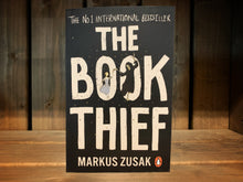Load image into Gallery viewer, Image of the front cover of The Book Thief. the cover is black, with the title in white text taking up most of the cover. Over the O&#39;s in &#39;Book&#39; is the illustration of a blonde girl dancing with Death.