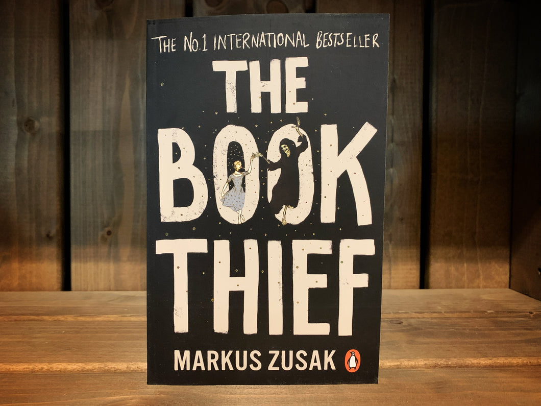 Image of the front cover of The Book Thief. the cover is black, with the title in white text taking up most of the cover. Over the O's in 'Book' is the illustration of a blonde girl dancing with Death.
